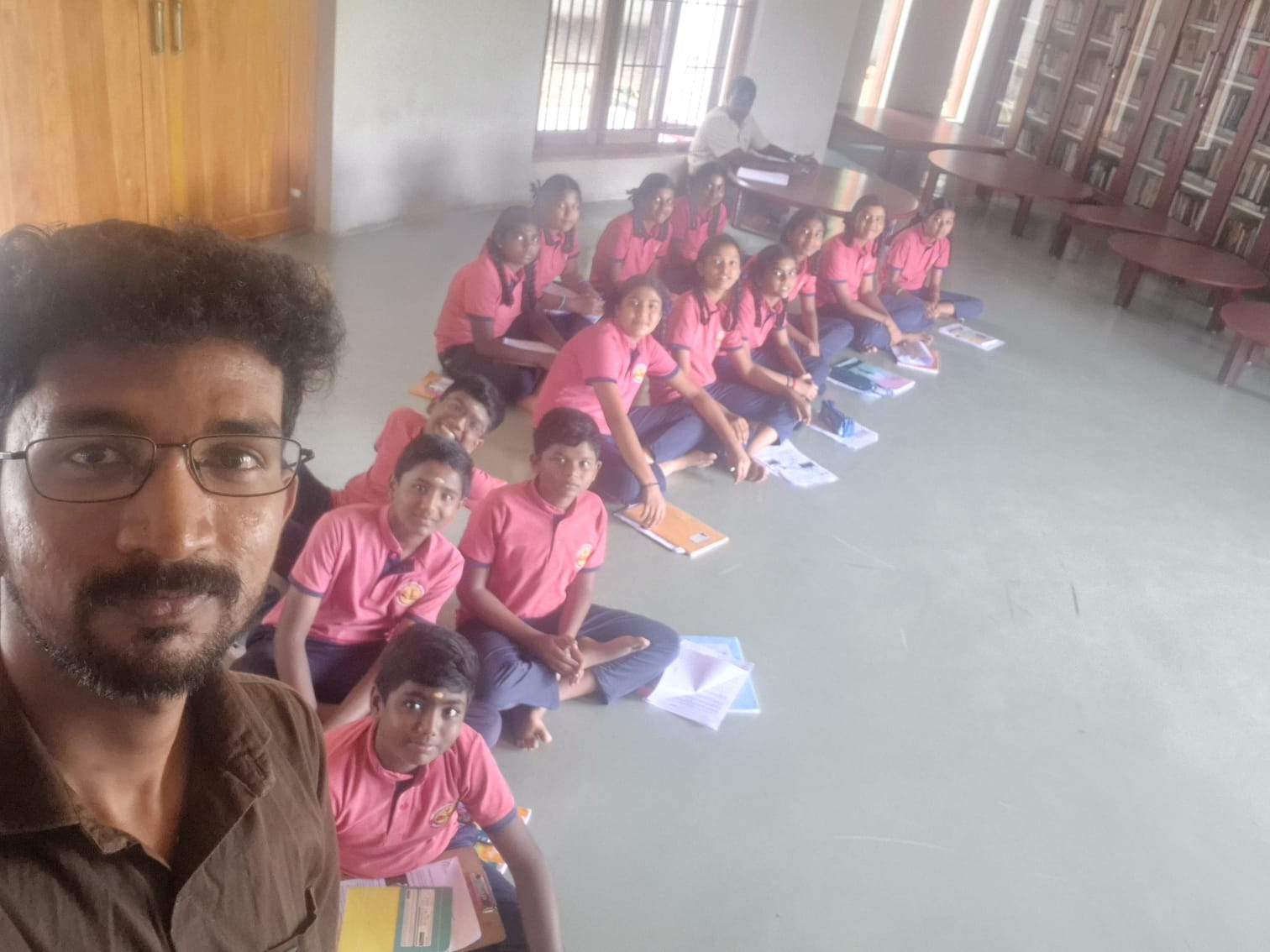 Students in pink uniforms sitting together with an educator in a candid group photograph